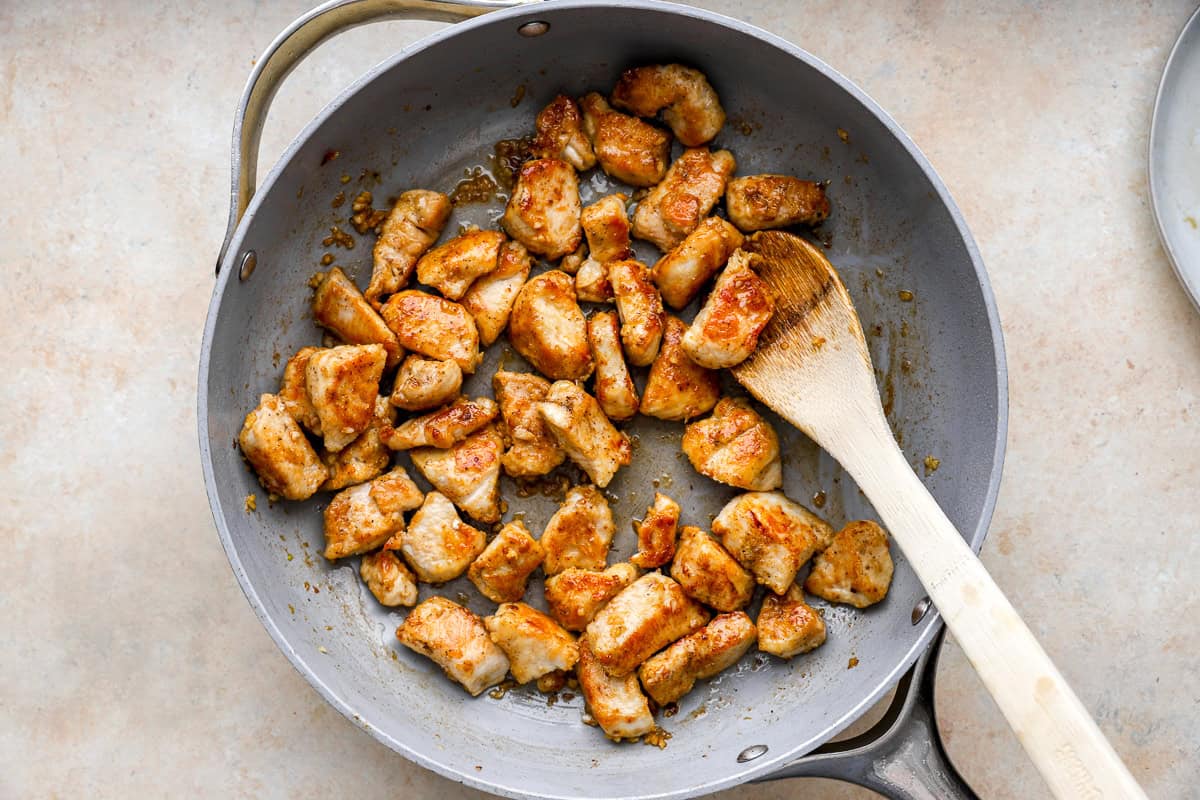 tossing chicken bites in garlic butter sauce with a wooden spoon.