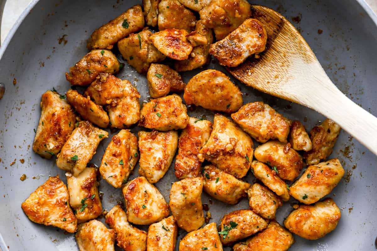 closeup partial overhead view of garlic butter chicken bites in a pan with a wooden spoon.