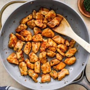 overhead view of garlic butter chicken bites in a pan with a wooden spoon.