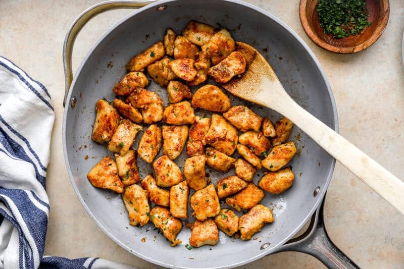 overhead view of garlic butter chicken bites in a pan with a wooden spoon.