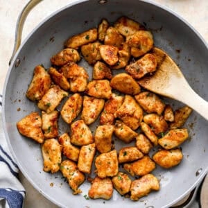 overhead view of garlic butter chicken bites in a pan with a wooden spoon.