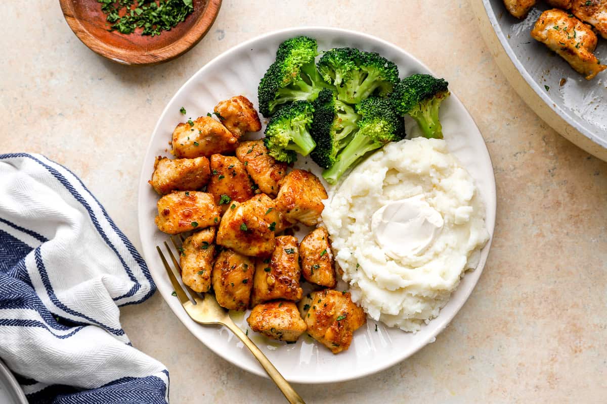 overhead view of a serving of garlic butter chicken bites on a white plate with mashed potatoes and broccoli.