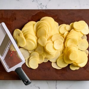 Yukon gold potato slices on a wooden cutting board with a mandoline slicer.