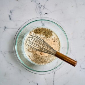 spices, seasonings, milk, and cream in a glass bowl with a whisk.