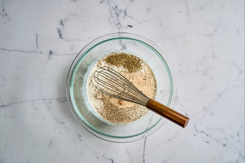spices, seasonings, milk, and cream in a glass bowl with a whisk.