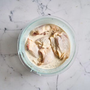 raw chicken thighs in a bowl with seasoned cream and milk.