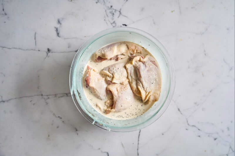 raw chicken thighs in a bowl with seasoned cream and milk.