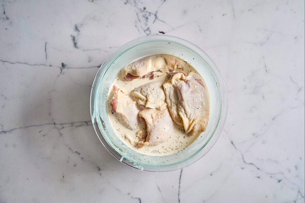 raw chicken thighs in a bowl with seasoned cream and milk.