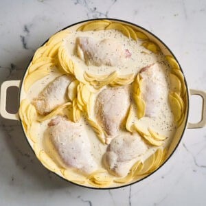 chicken thighs and potato slices arranged in a braiser and topped with seasoned cream.