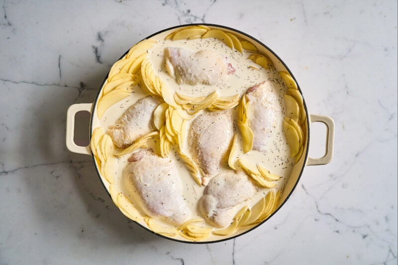 chicken thighs and potato slices arranged in a braiser and topped with seasoned cream.