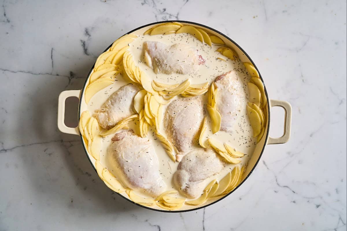 chicken thighs and potato slices arranged in a braiser and topped with Dijon cream.