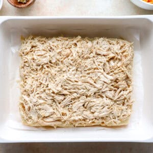 bottom slider rolls topped with ranch shredded chicken in a baking pan.