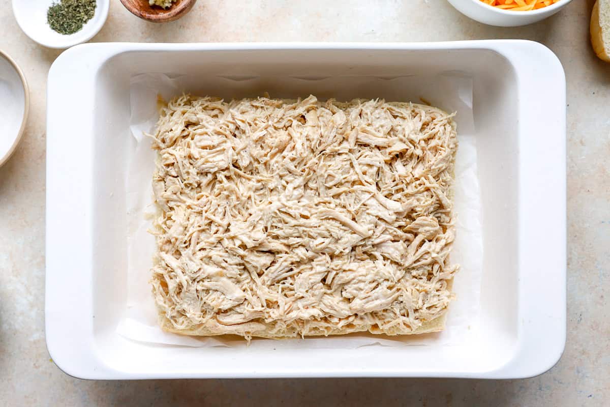 bottom slider rolls topped with ranch shredded chicken in a baking pan.