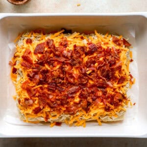 crumbled bacon and shredded cheddar cheese over chicken-topped slider rolls in a baking dish.