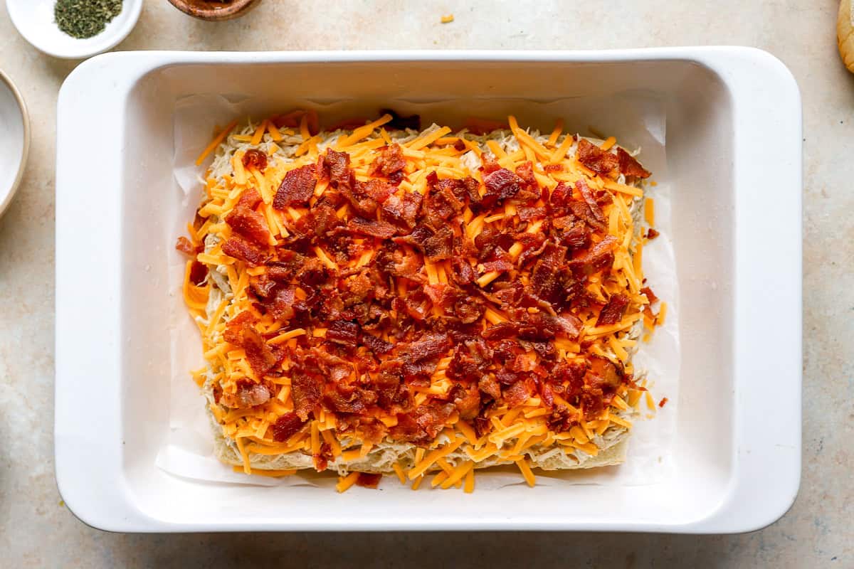 crumbled bacon and shredded cheddar cheese over chicken-topped slider rolls in a baking dish.