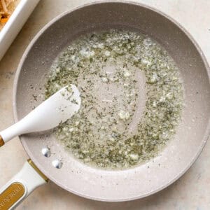 melted butter with herbs and garlic in a pan with a rubber spatula.