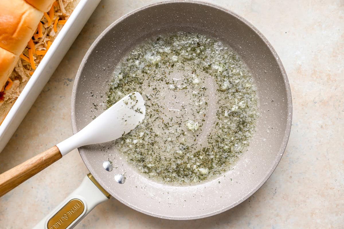 melted butter with herbs and garlic in a pan with a rubber spatula.