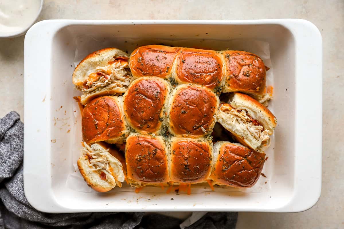 overhead view of chicken bacon ranch sliders in a baking dish; three are turned on their sides to show the filling.