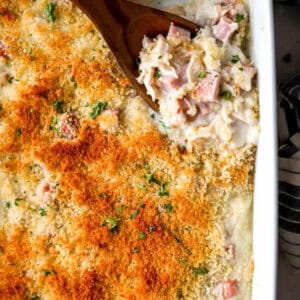 Wooden spoon scooping cup a portion of chicken cordon bleu casserole out of a dish.