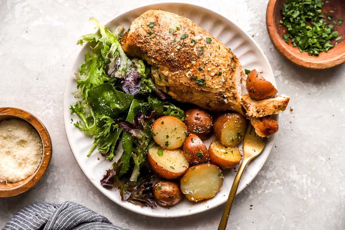 overhead view of a crockpot chicken breast and potatoes on a white plate with a side salad and a fork.
