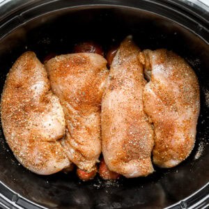 seasoned raw chicken breasts over red baby potatoes in a crockpot.