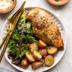 overhead view of a crockpot chicken breast and potatoes on a white plate with a side salad and cutlery.