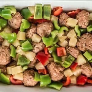 Meatballs, chopped bell peppers, and pineapple in a dish, before baking.