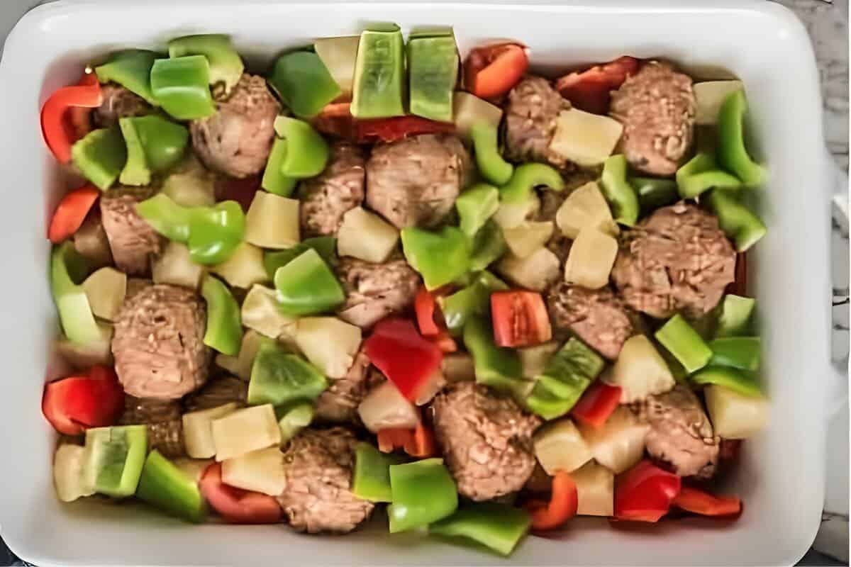 Meatballs, chopped bell peppers, and pineapple in a dish, before baking.