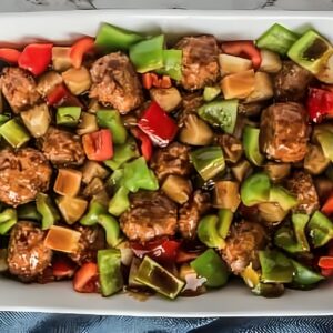 Meatballs, bell peppers, and pineapple in a baking dish, coated with sauce.