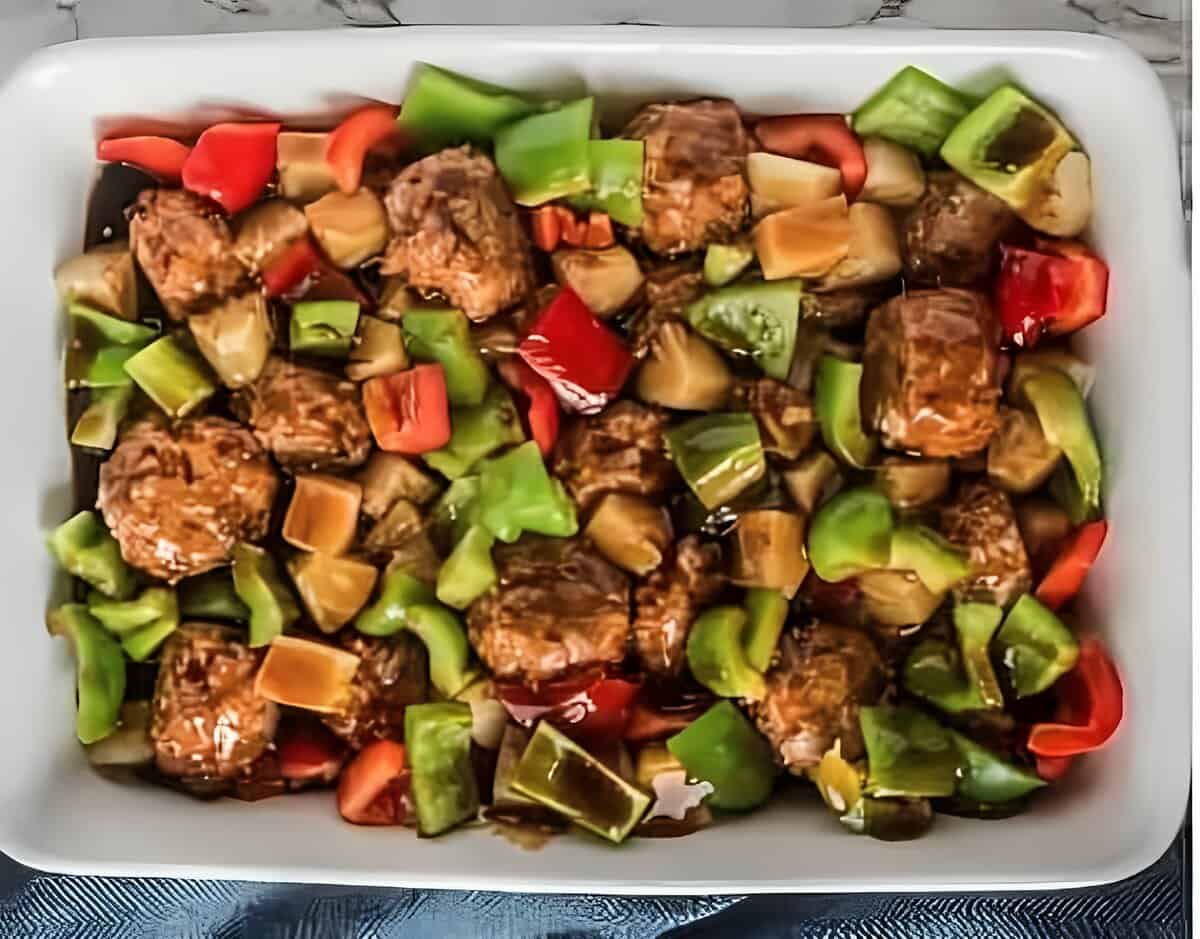 Meatballs, bell peppers, and pineapple in a baking dish, coated with sauce.