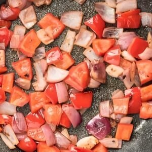 Chopped peppers and onions cooking in a skillet.