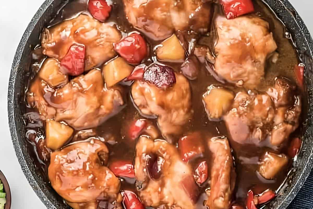 Chicken thighs, pineapple, peppers, and onions cooking in sauce.
