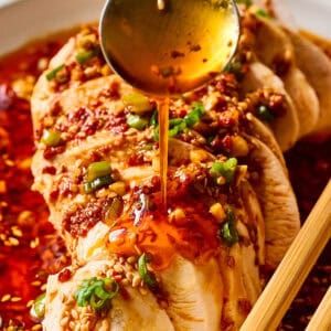 spooning sauce over a sliced mouthwatering chicken breast on a white plate.