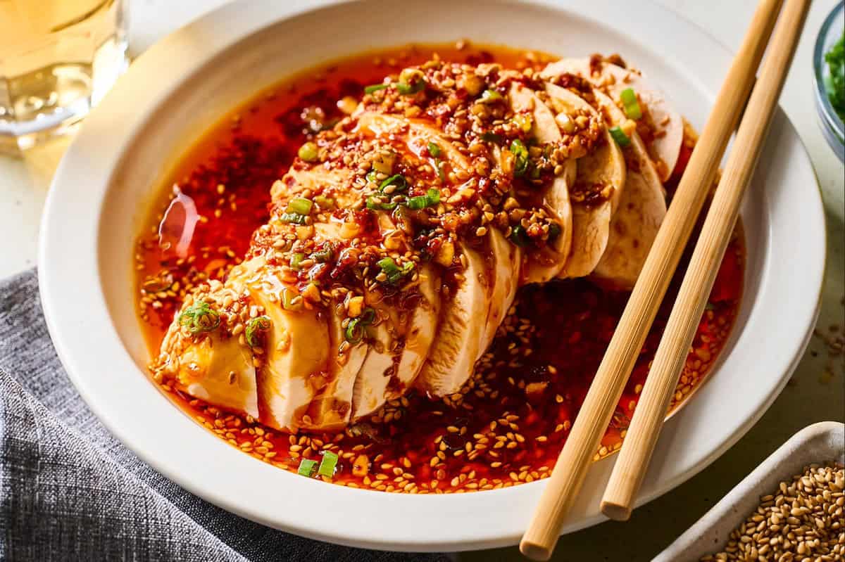 a sliced poached chicken breast with chili sauce, on a white plate with chopsticks.