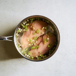 raw chicken breasts in a saucepan of water, scallions, ginger, and salt.