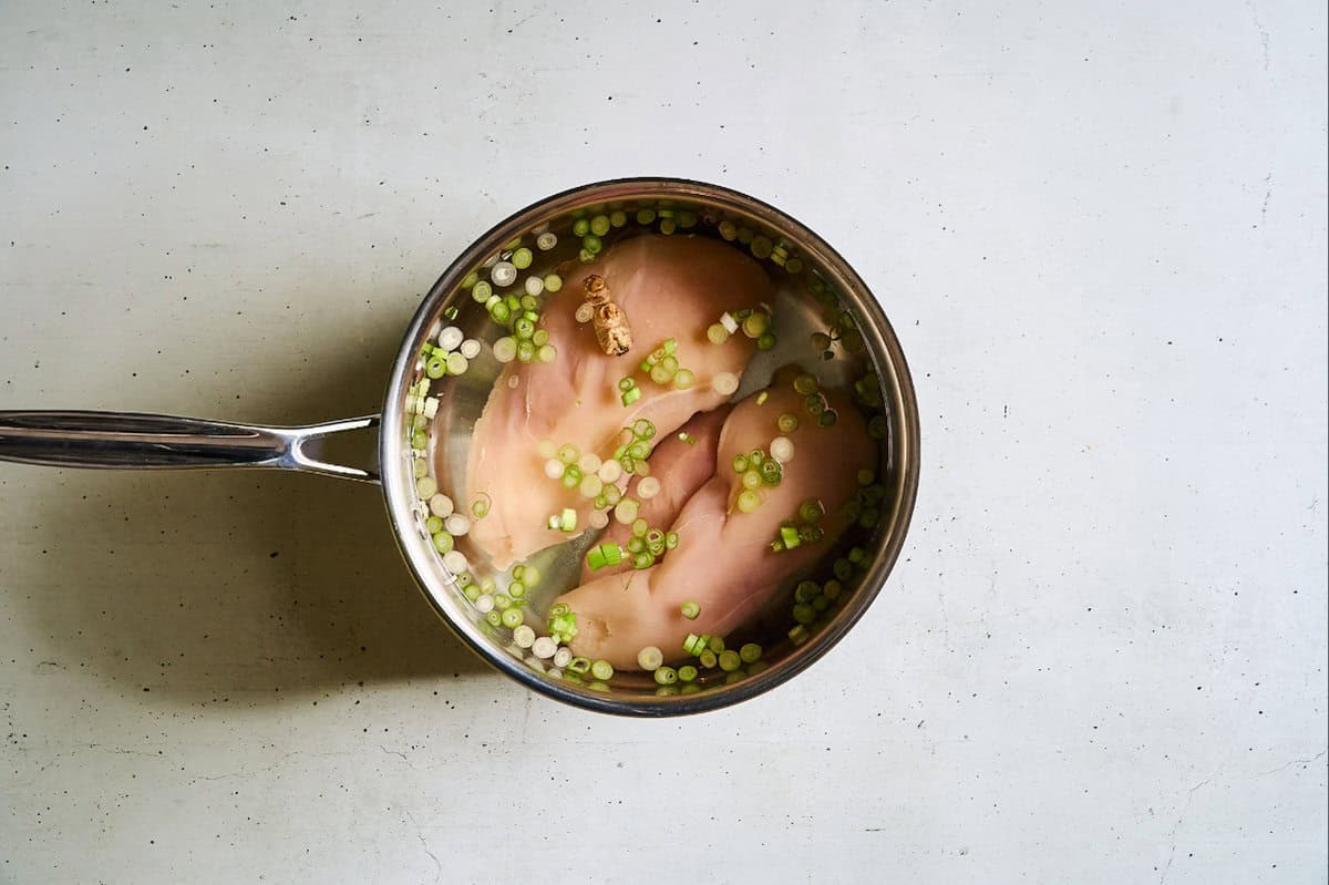 raw chicken breasts in a saucepan of water, scallions, ginger, and salt.