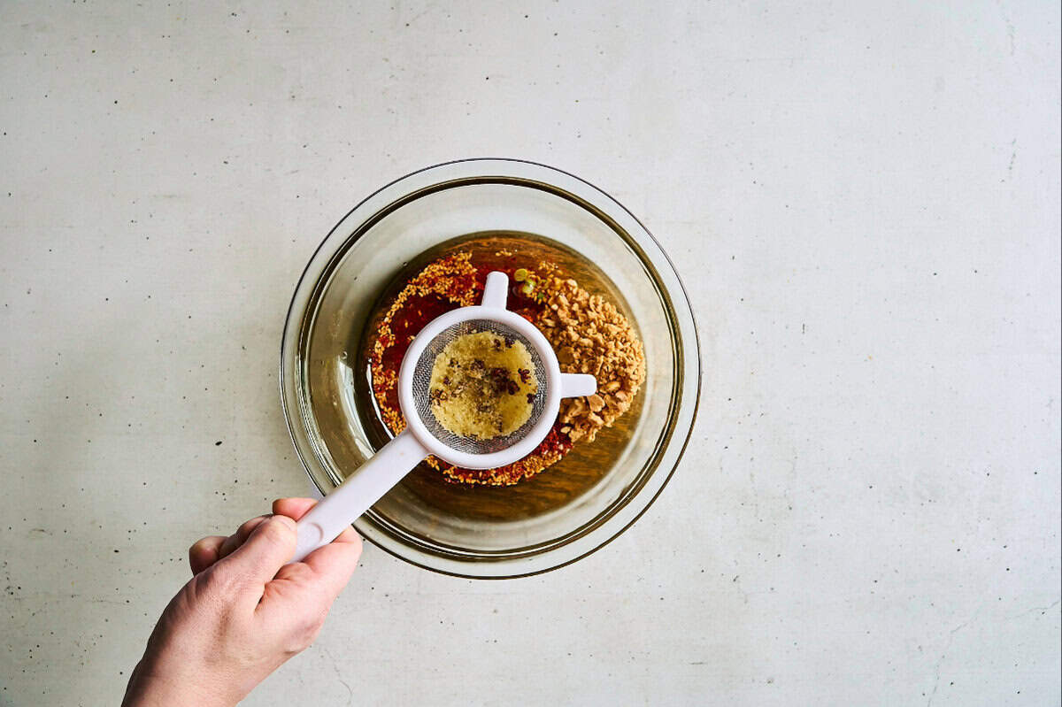 straining the solids from fragrant oil over spices in a bowl.