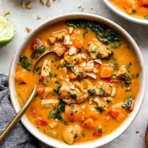 overhead view of a bowl of peanut chicken soup with a spoon.