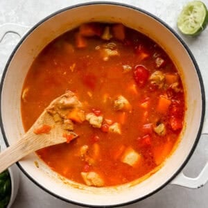 cooking peanut chicken soup in a dutch oven with a wooden spoon.