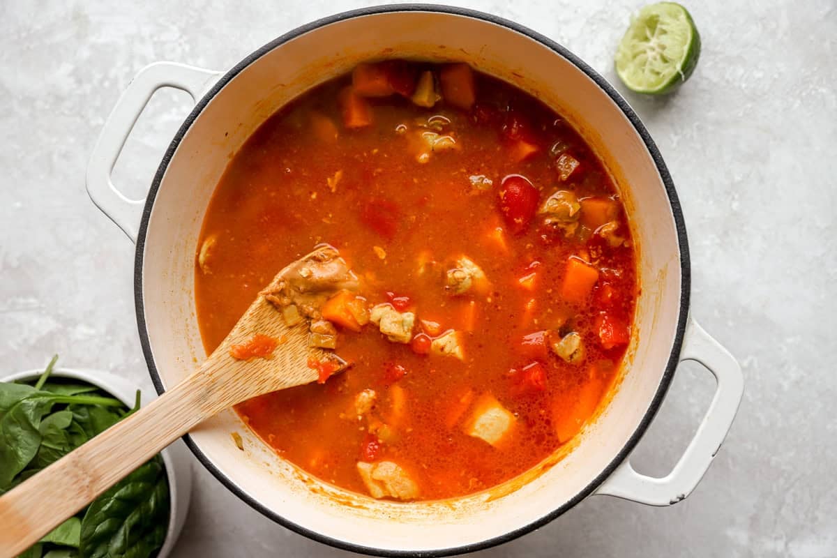 cooking peanut chicken soup in a dutch oven with a wooden spoon.