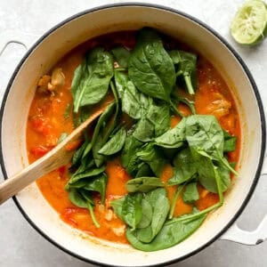 stirring spinach into peanut chicken soup with a wooden spoon.