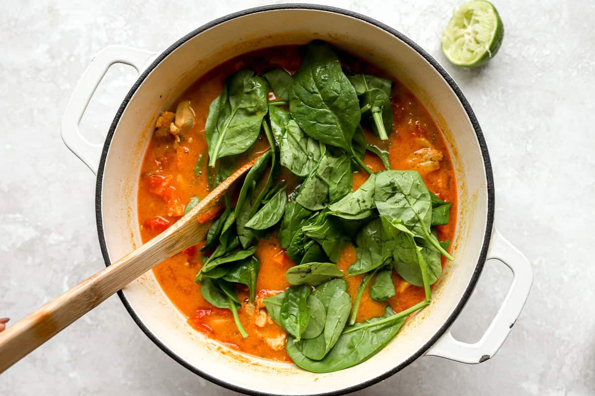 stirring spinach into peanut chicken soup with a wooden spoon.