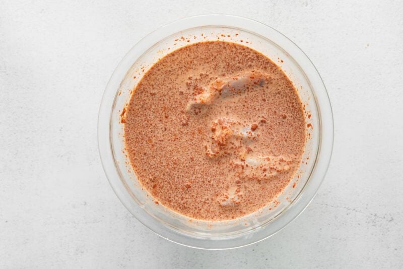 raw chicken wings marinating in nashville hot brine in a glass bowl.
