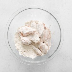 tossing marinated chicken wings in flour in a glass bowl.