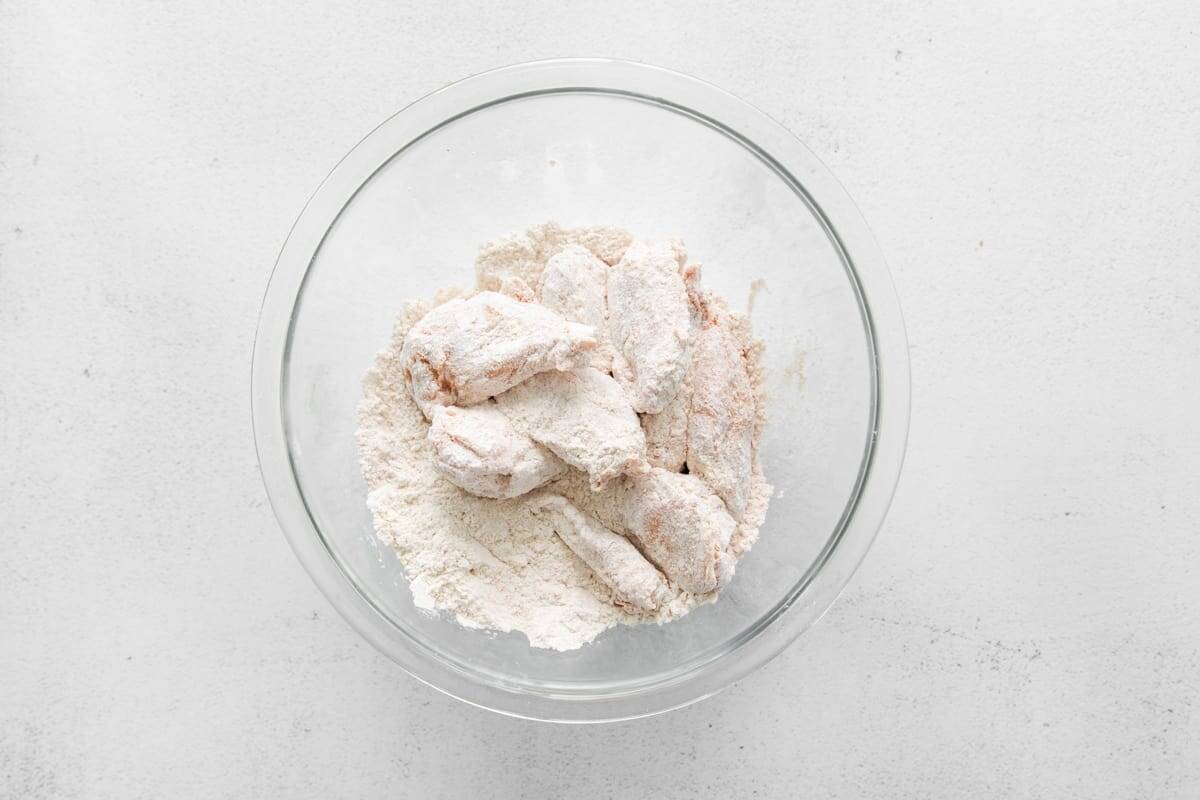 tossing marinated chicken wings in flour in a glass bowl.