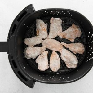 seasoned floured raw chicken wings in an air fryer basket.