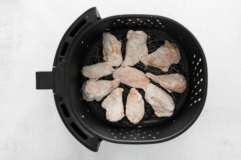 seasoned floured raw chicken wings in an air fryer basket.