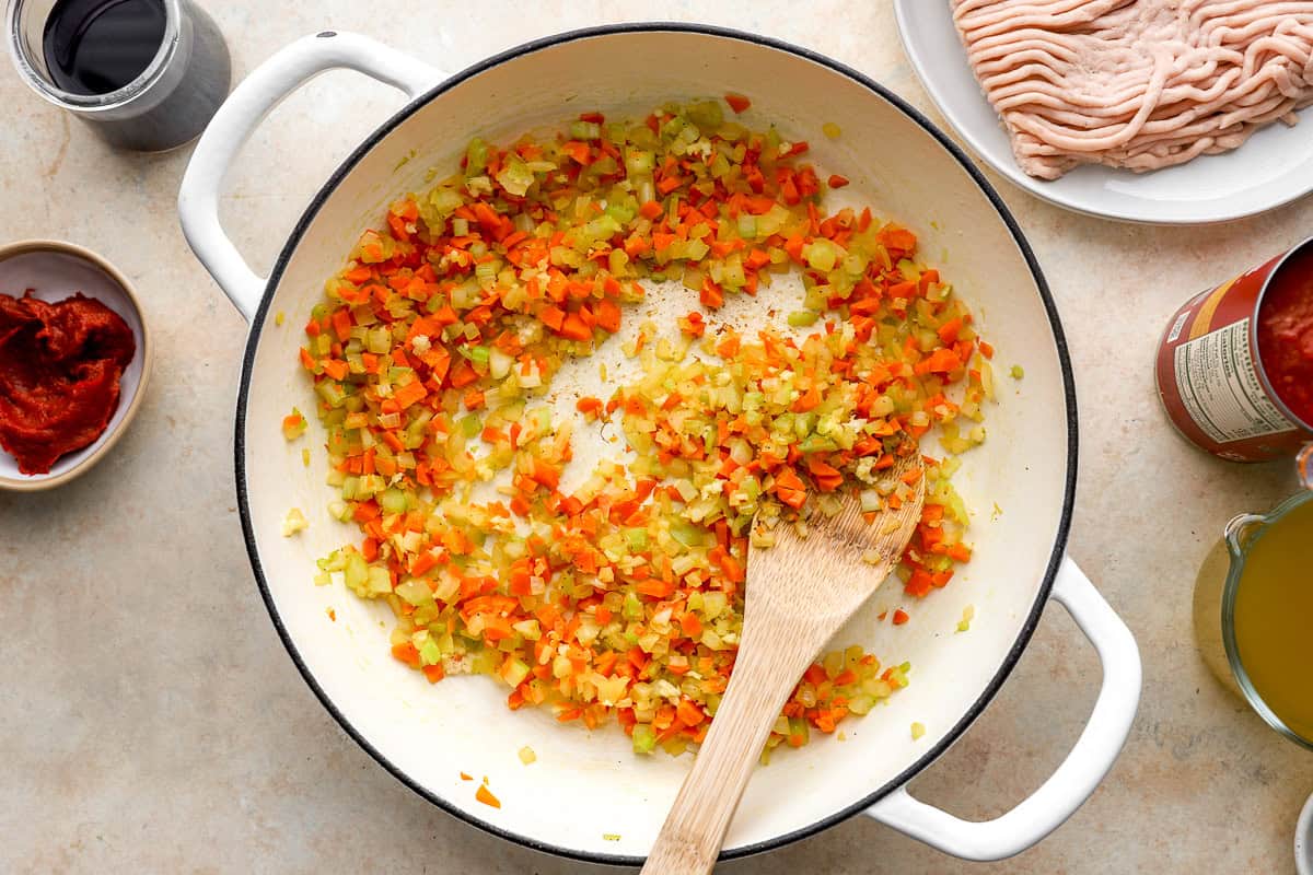 sauteeing mirepoix in a dutch oven with a wooden spoon.