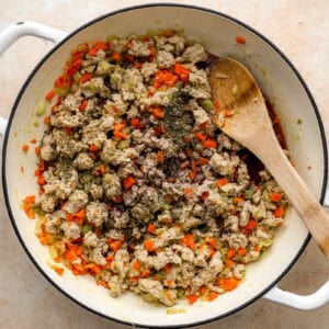 cooking ground chicken and mirepoix in a dutch oven with a wooden spoon.