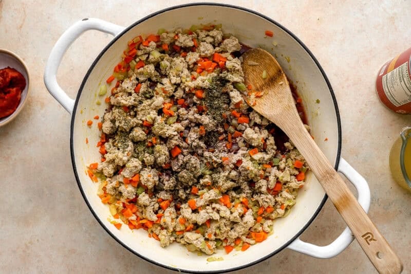 cooking ground chicken and mirepoix in a dutch oven with a wooden spoon.